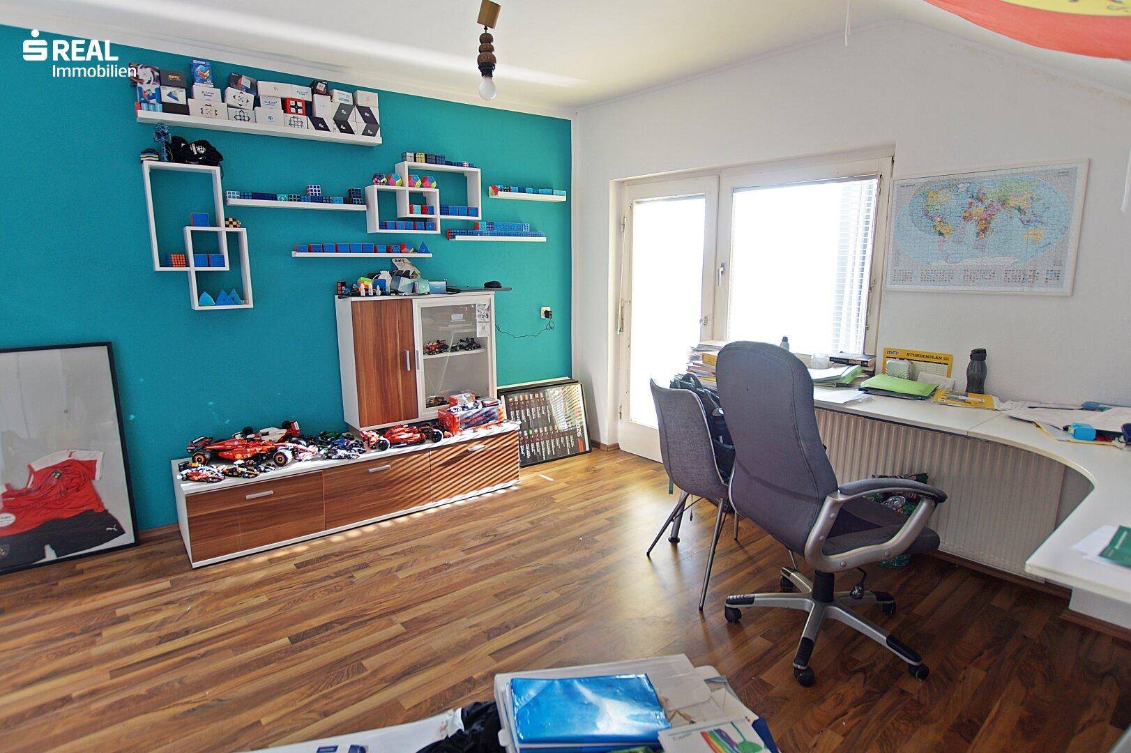 Arbeitszimmer mit Schreibtisch, bunten Regalen und Zugang zu einem Balkon.