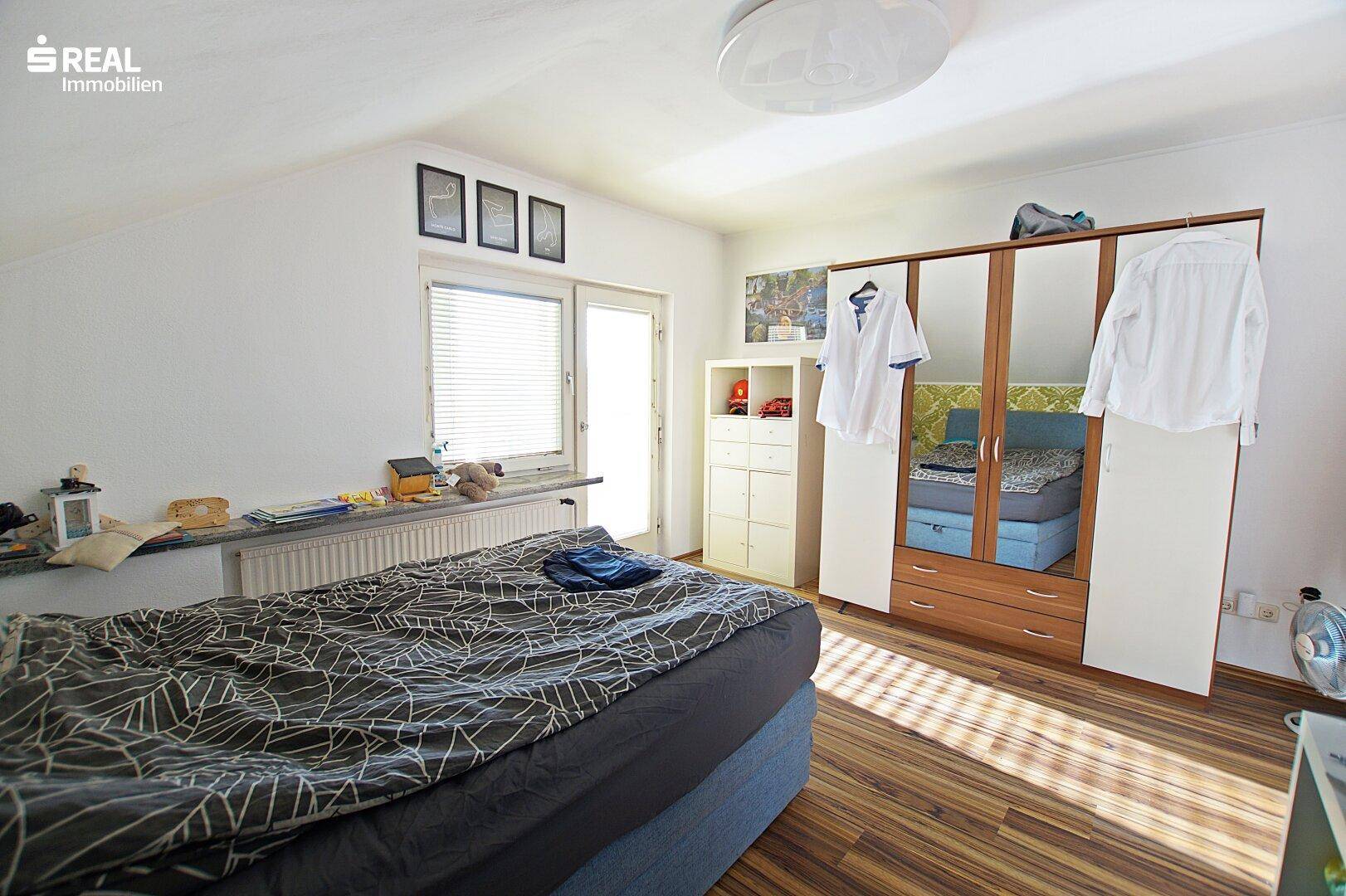 Helles Schlafzimmer im Dachgeschoss mit großem Kleiderschrank und Fenster.