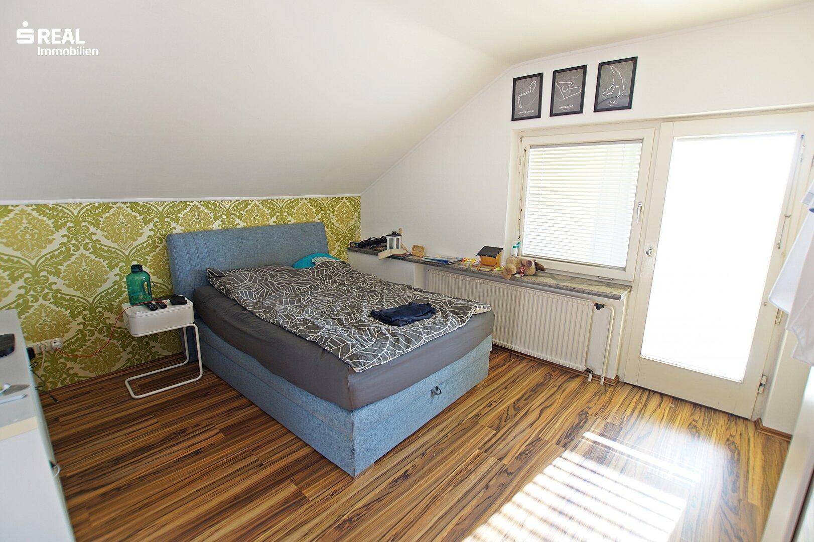 Schlafzimmer im Dachgeschoss mit schräger Decke, Doppelbett und Holzboden.
