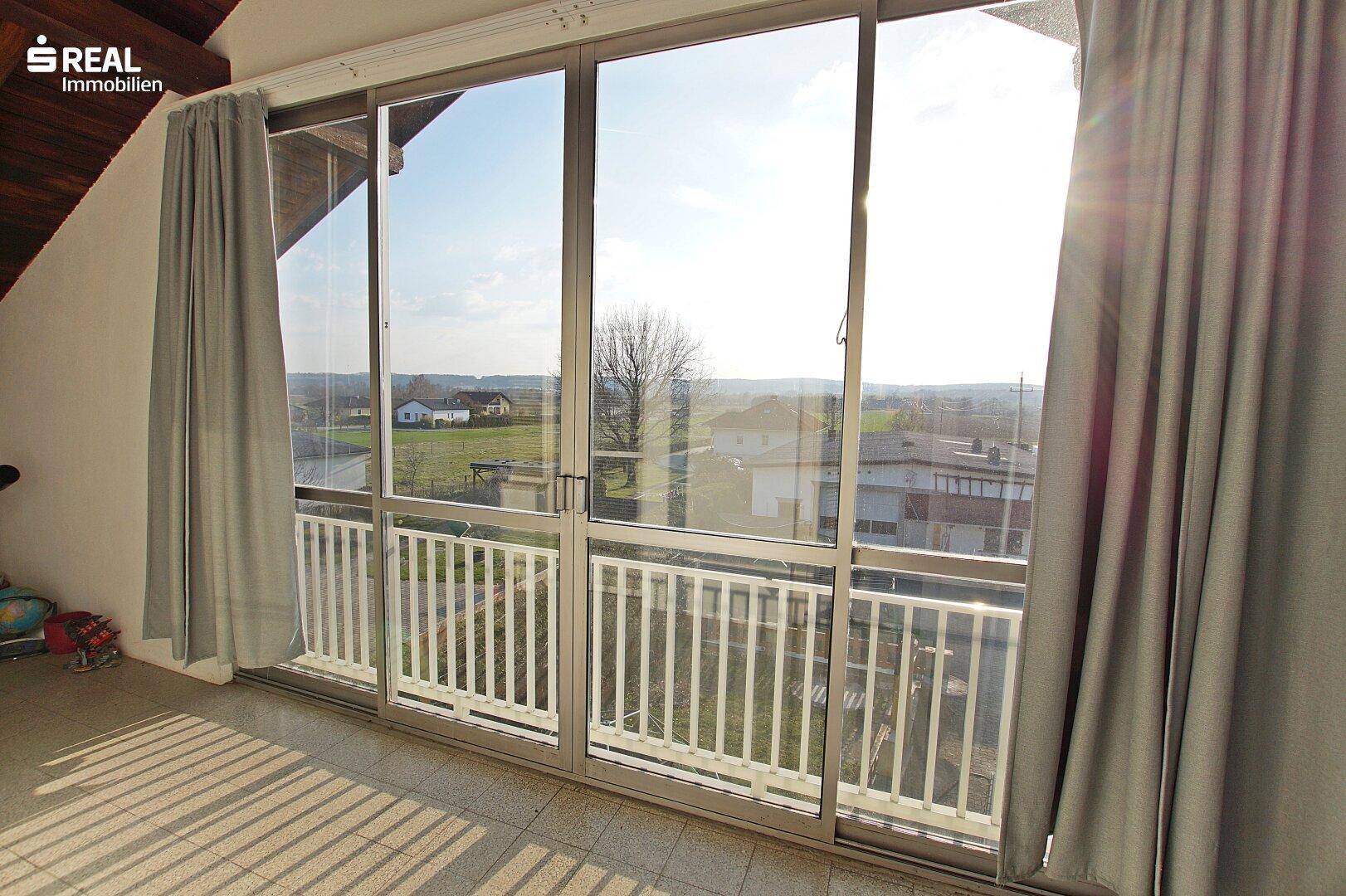Heller Balkon mit weitem Blick über die Landschaft und große Fensterfront.