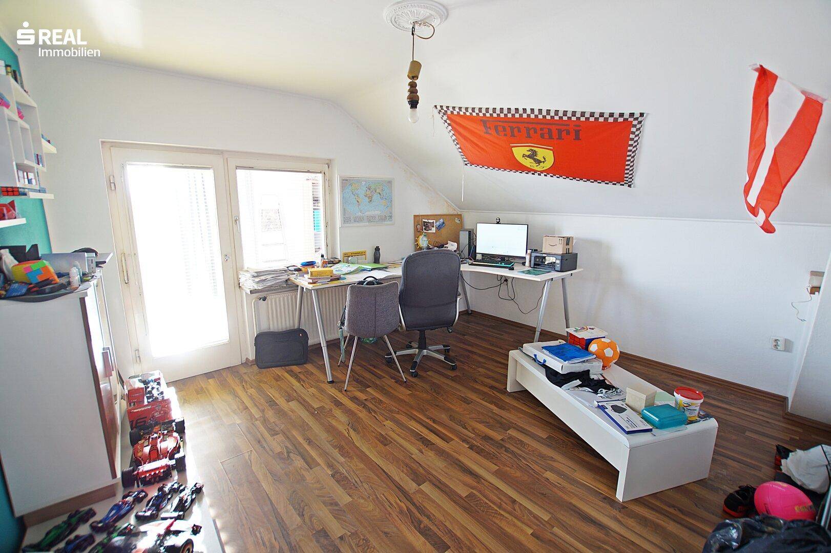 Geräumiges Arbeitszimmer im Dachgeschoss mit Schreibtisch und Fensterfront.