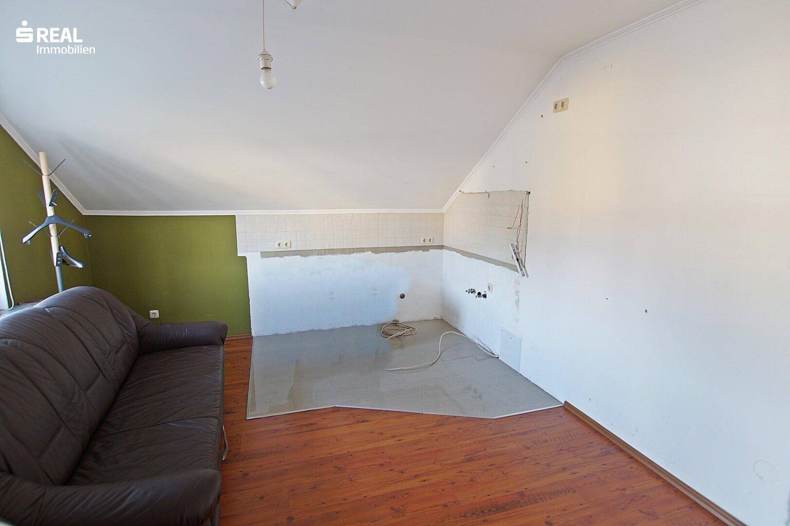 Unfertiger Raum im Dachgeschoss mit vorbereiteten Anschlüssen für eine Küche.