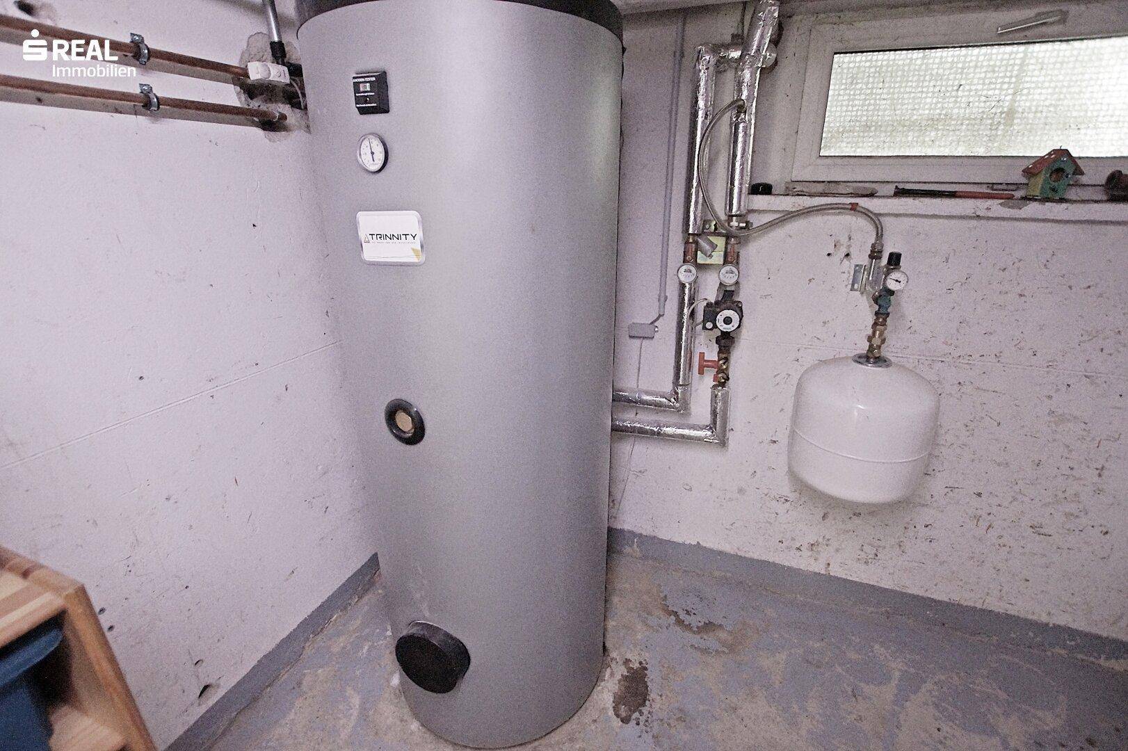 Heizraum mit großem Warmwasserspeicher und sichtbaren Rohrleitungen.