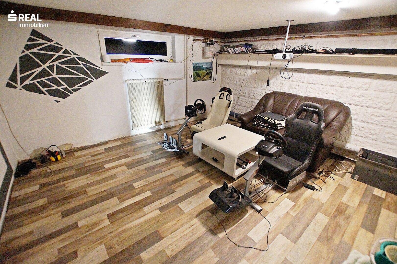 Hobbyraum im Keller mit Gaming-Setup, Sofa und dekorativer Wandgestaltung.