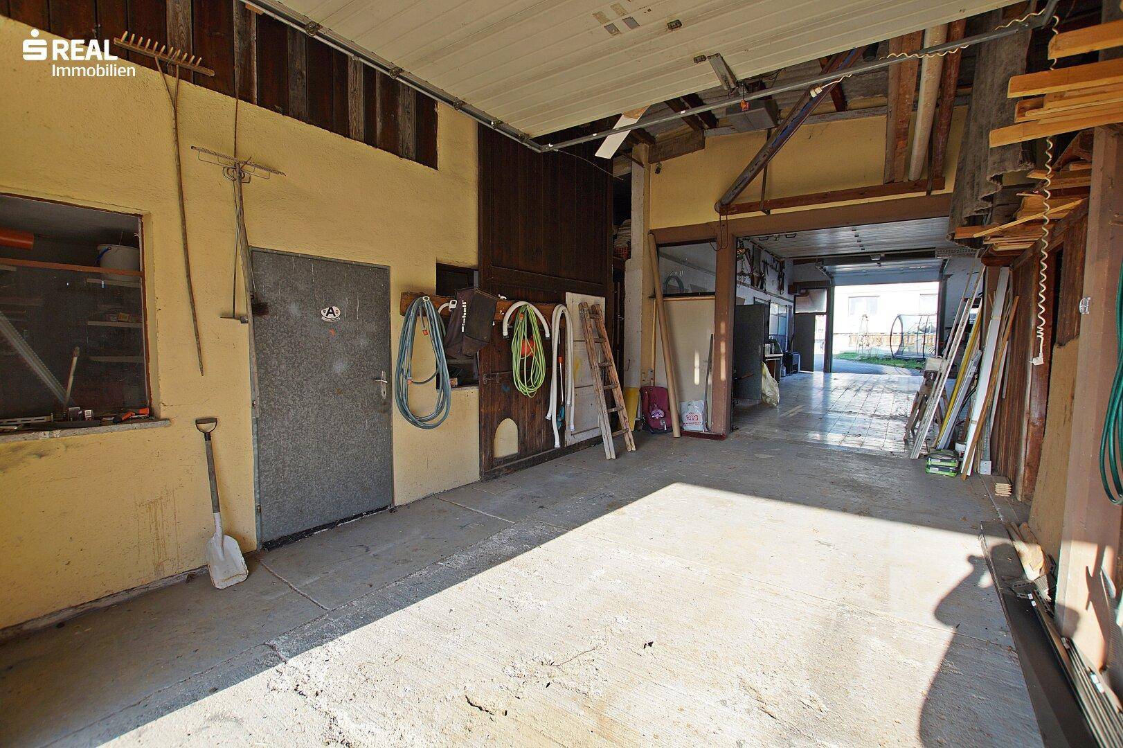 Große Garage mit Betonboden, Werkzeugen und Zugang zum Außenbereich.