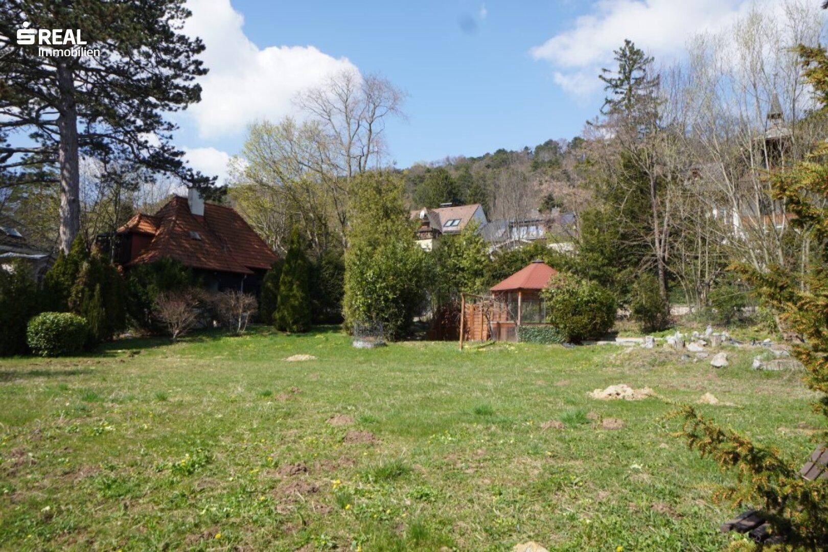 Blick auf das Haus und den weitläufigen Garten mit einem kleinen Pavillon unter blauem Himmel.