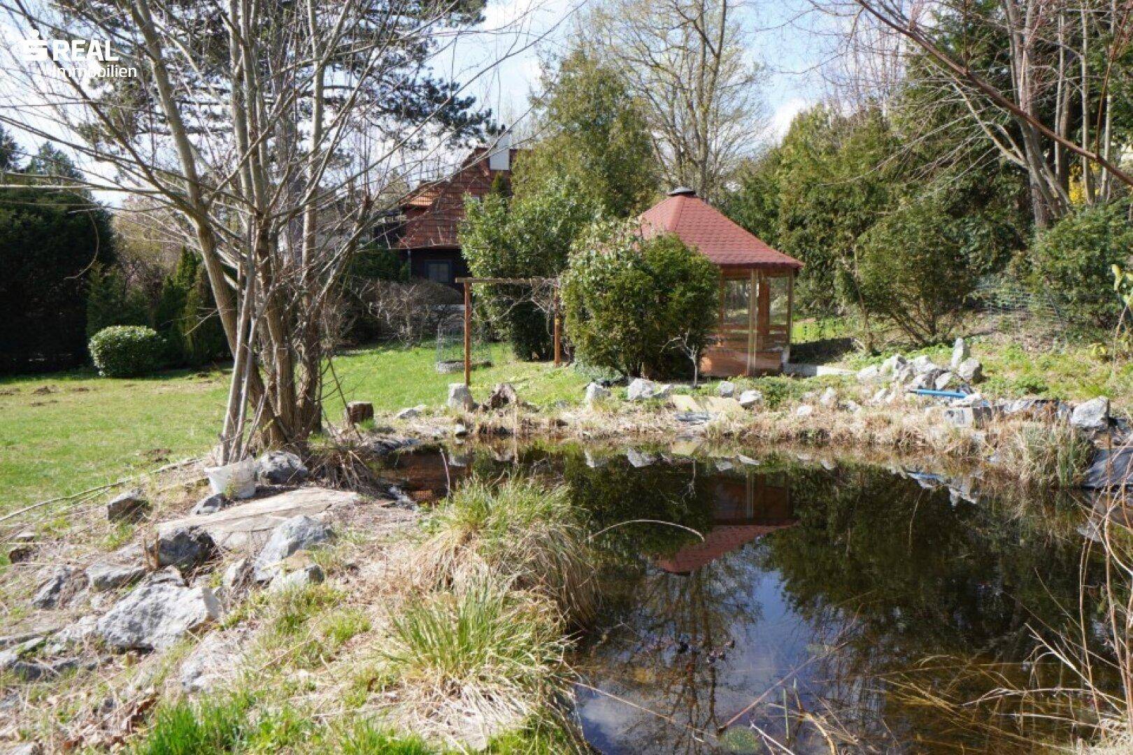 Natürlicher Gartenteich mit Felsen und einem charmanten Gartenpavillon im Hintergrund.