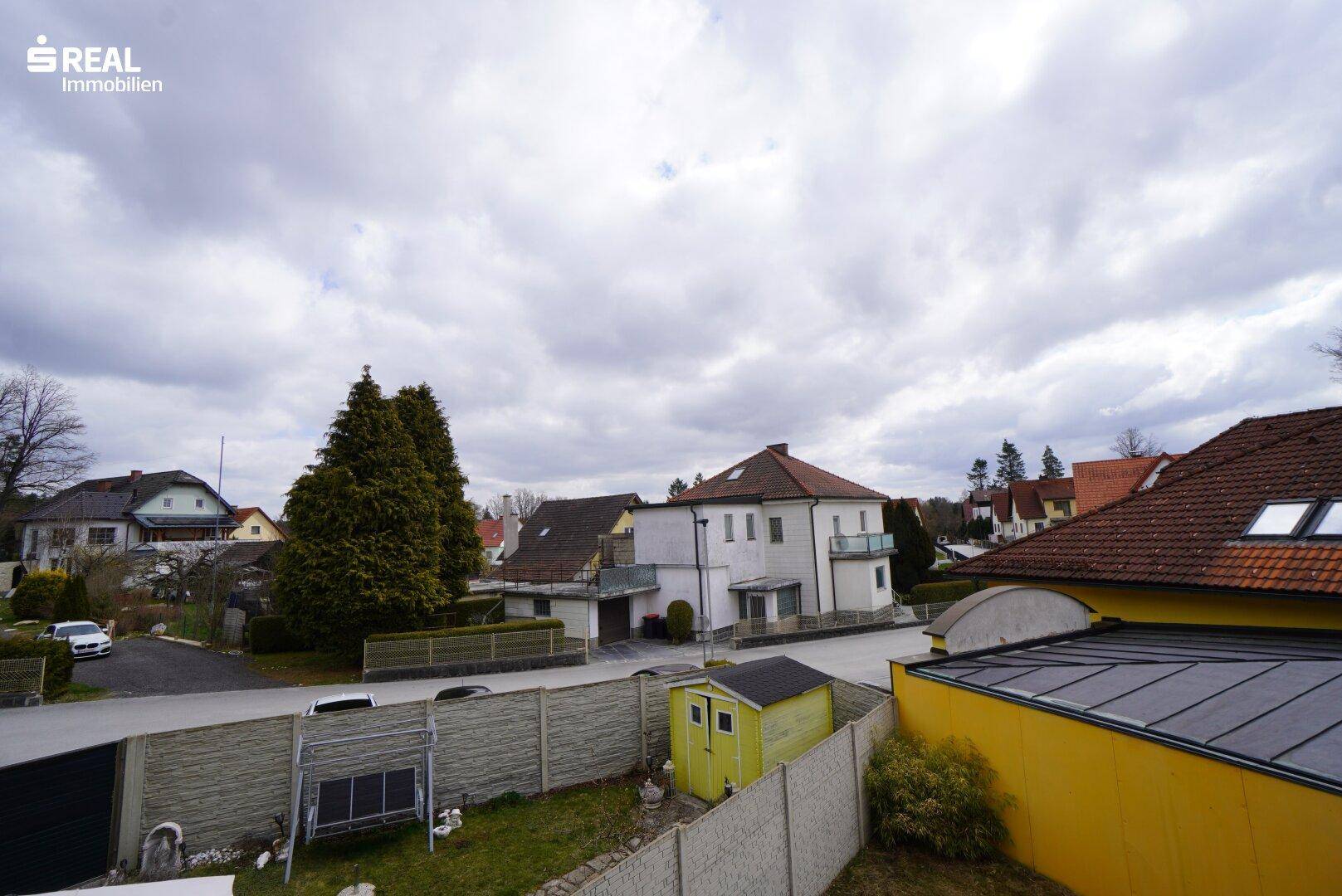 Blick über die Nachbarschaft mit Wohnhäusern und Gärten unter bewölktem Himmel.