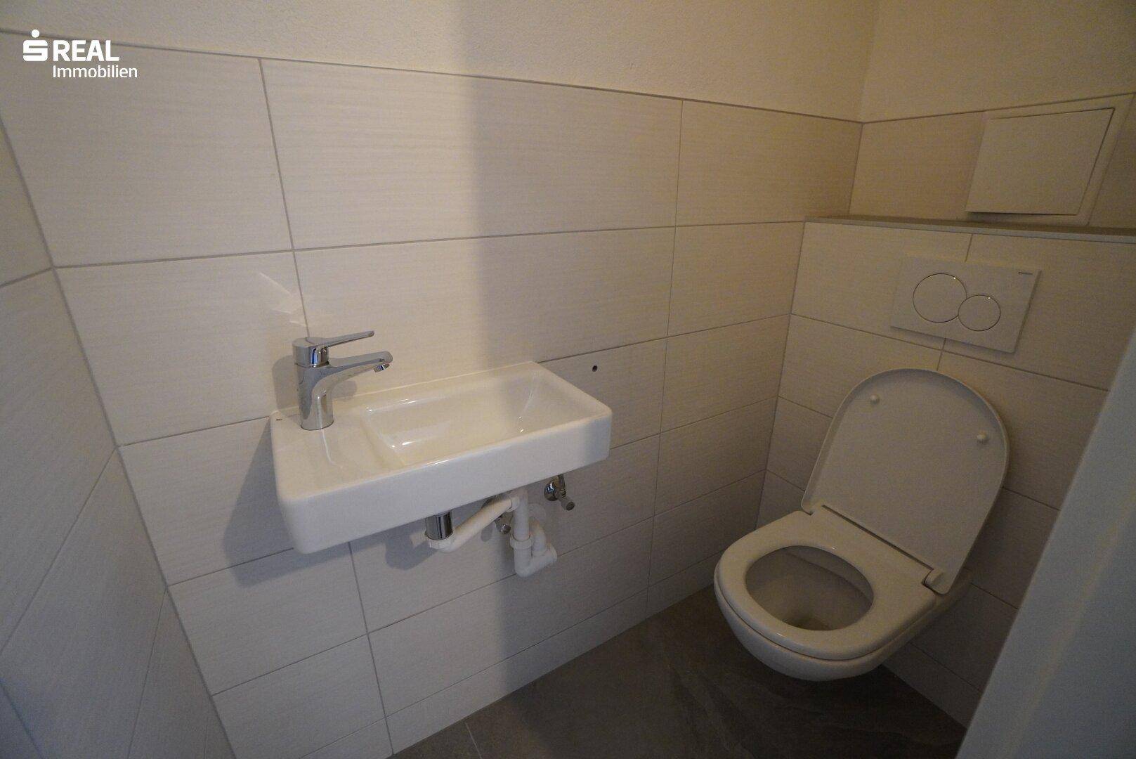 Kleines Gäste-WC mit Wand-WC, Waschbecken und hellen Fliesen.