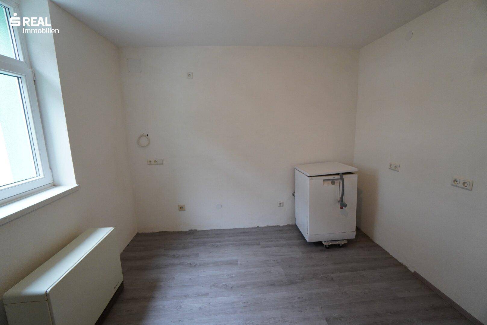 Leerer Raum mit Fenster, Laminatboden und Anschlussmöglichkeiten.