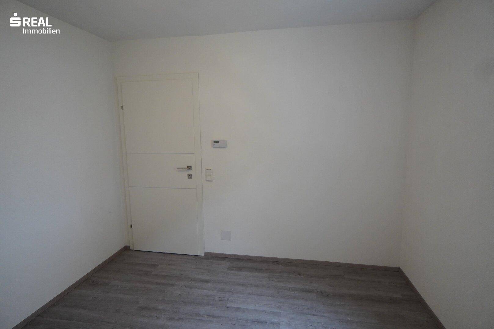Leerer Raum mit Tür und Laminatboden, ideal als Schlaf- oder Arbeitszimmer.