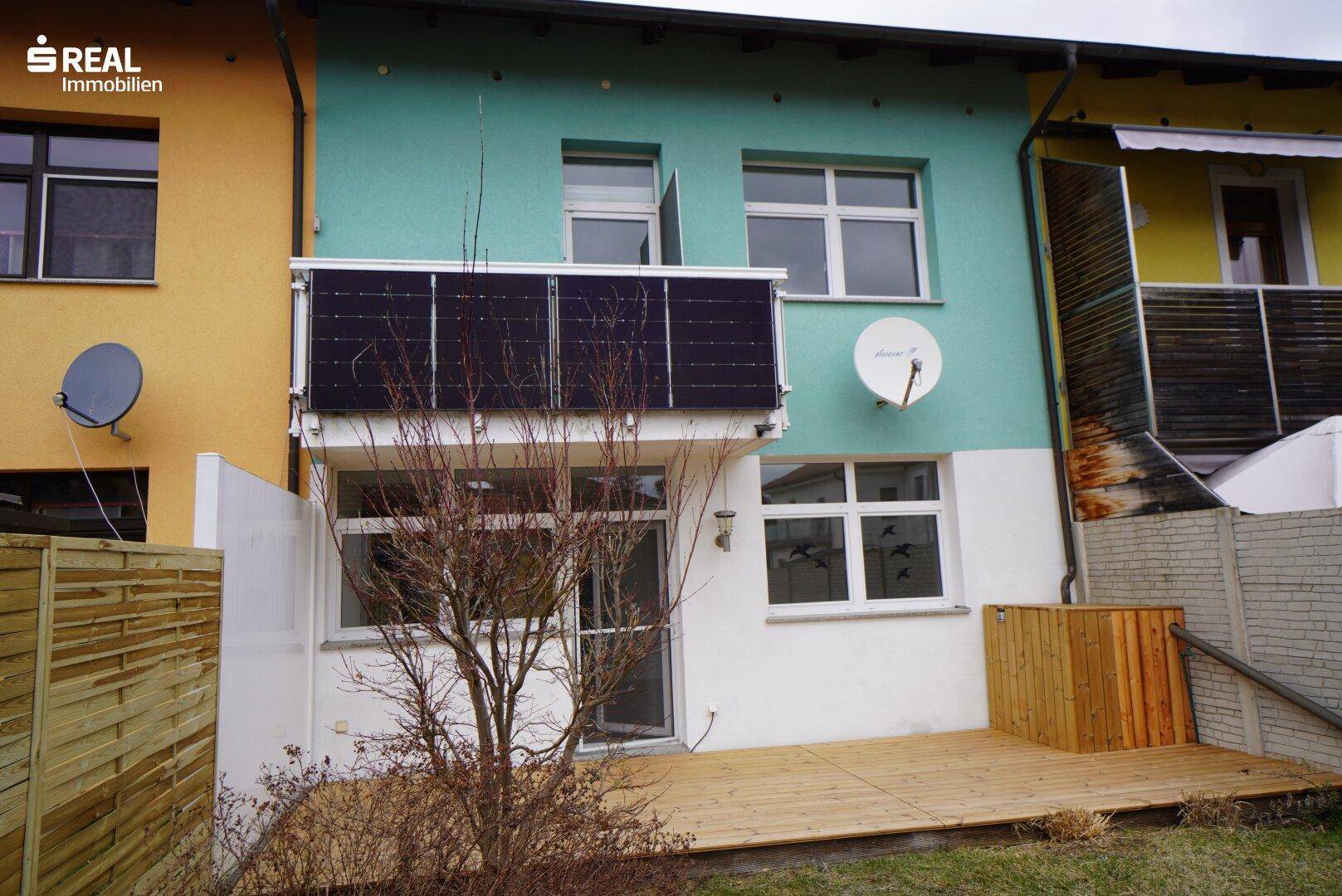 Rückansicht des Hauses mit Holzterrasse, Solarpaneelen und Garten.