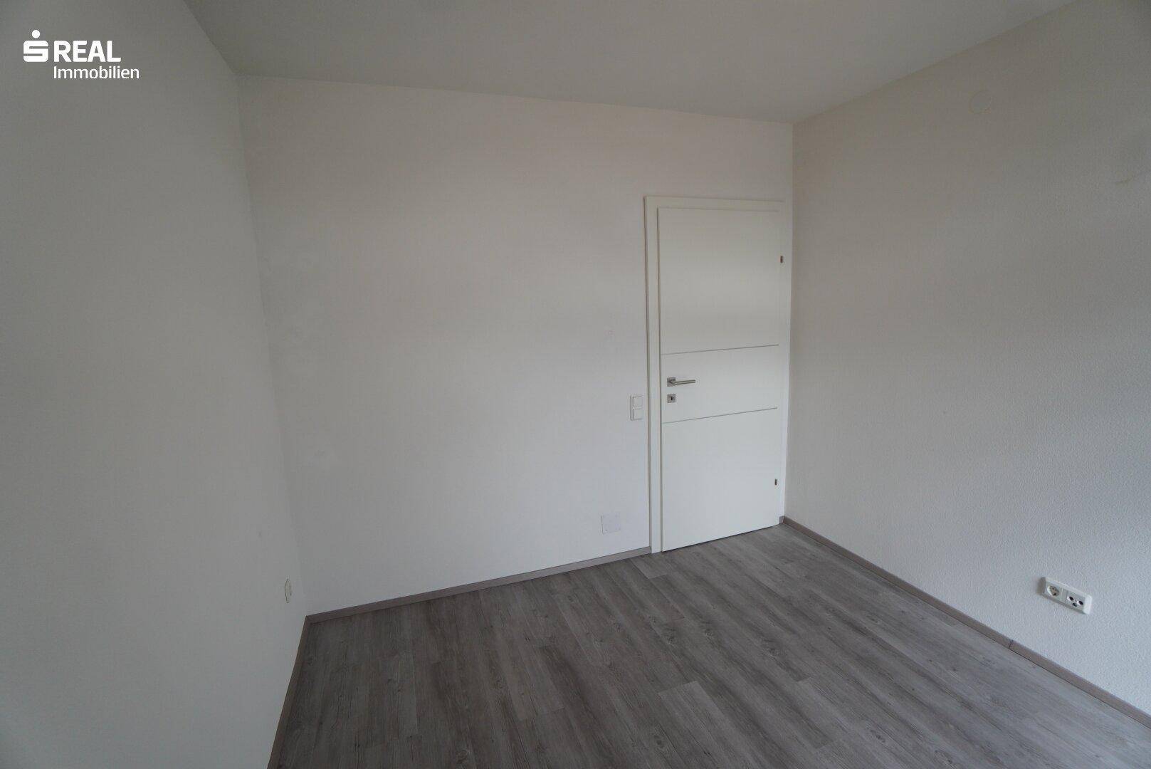 Leeres Schlafzimmer mit Laminatboden und weiß gestrichenen Wänden.