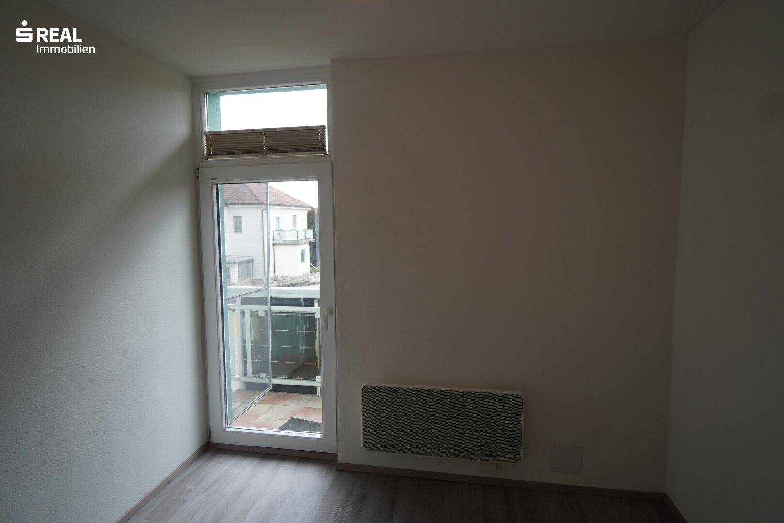 Schlafzimmer mit Zugang zum Balkon und Heizkörper unter dem Fenster.