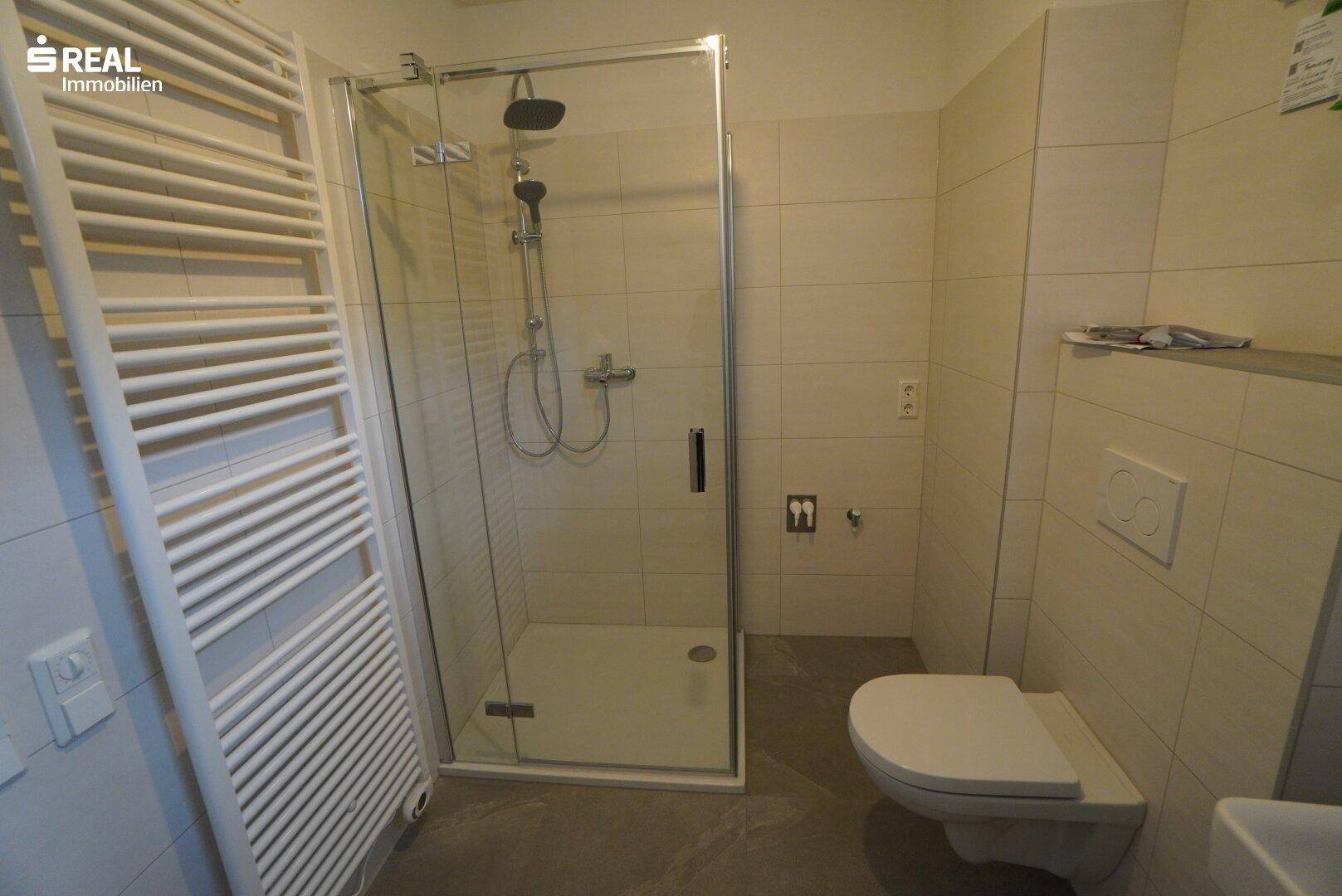 Modernes Badezimmer mit Duschkabine, WC und beheiztem Handtuchhalter.