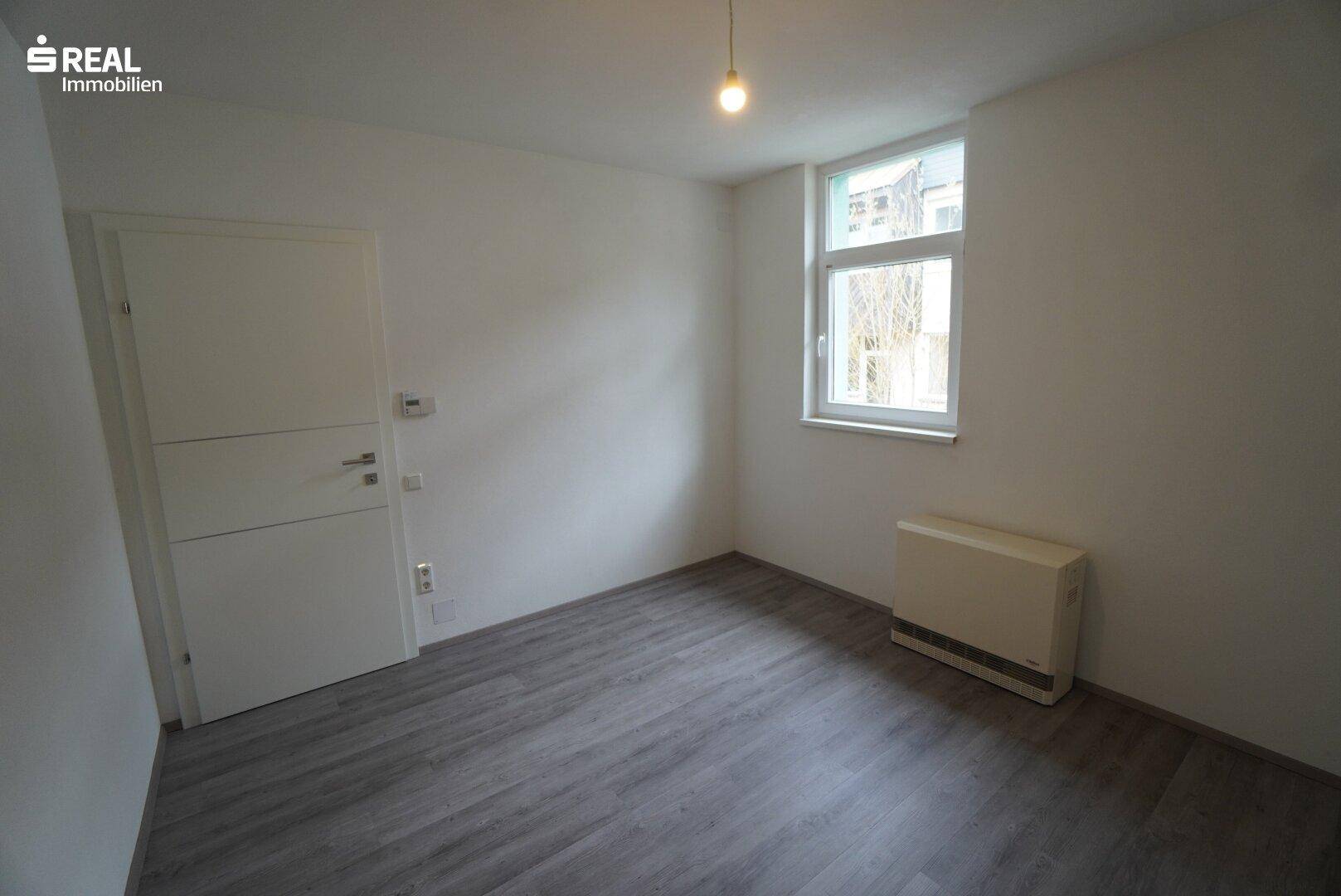Leeres Schlafzimmer mit Laminatboden und Fenster, bereit zur Einrichtung.