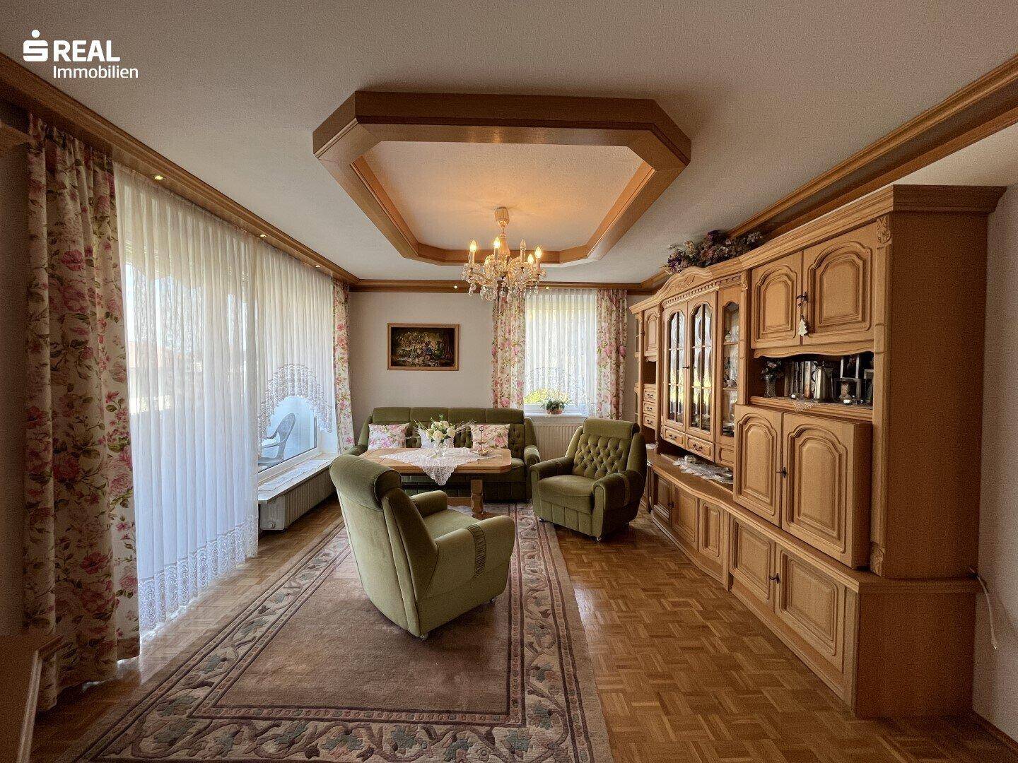 Geräumiges Wohnzimmer mit traditionellen Holzmöbeln, Parkettboden und Kronleuchter.