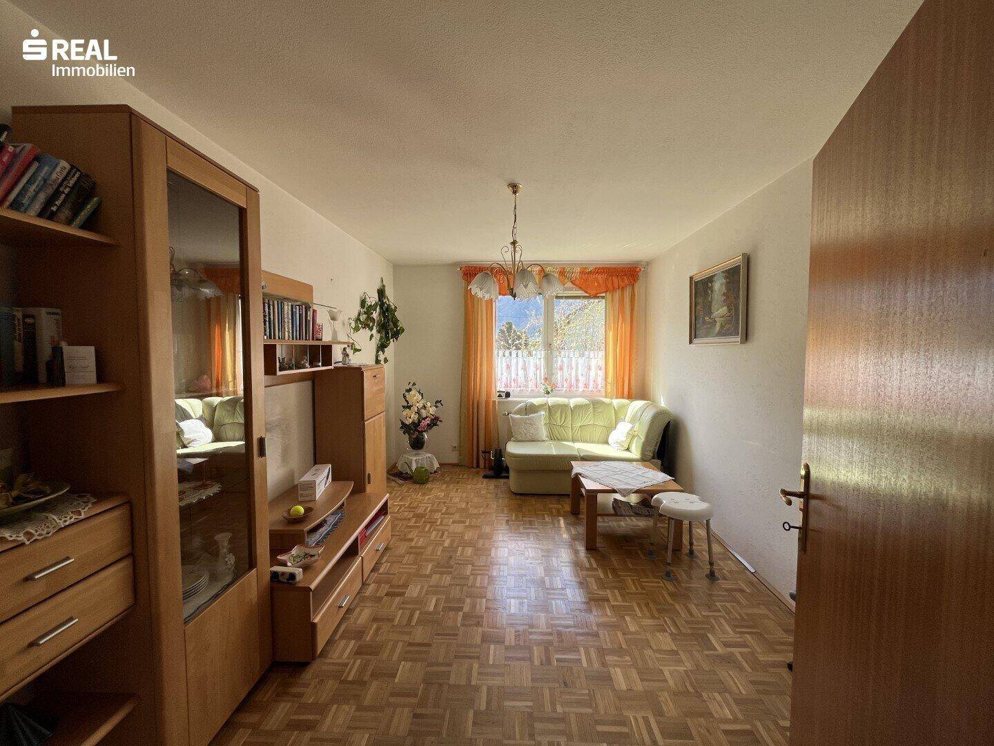 Helles Wohnzimmer mit Parkettboden, großem Fenster und traditionellen Möbeln.