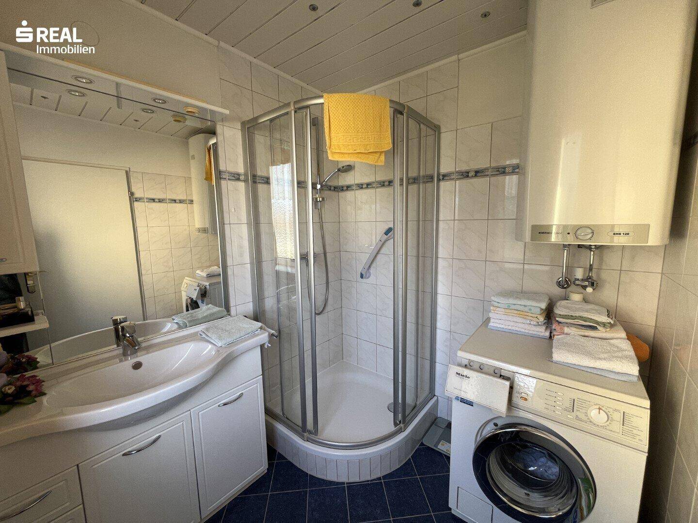 Gefliestes Badezimmer mit Duschkabine, Waschbecken und Waschmaschine.
