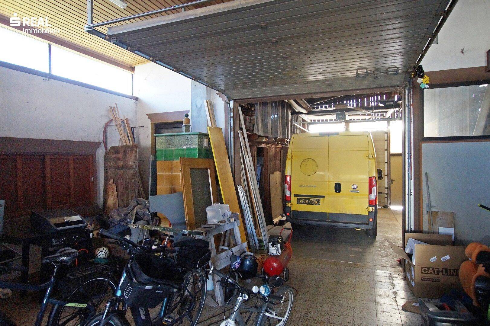Geräumige Garage mit einem gelben Lieferwagen, Fahrrädern und verschiedenen Lagergegenständen, beleuchtet durch ein Oberlicht.