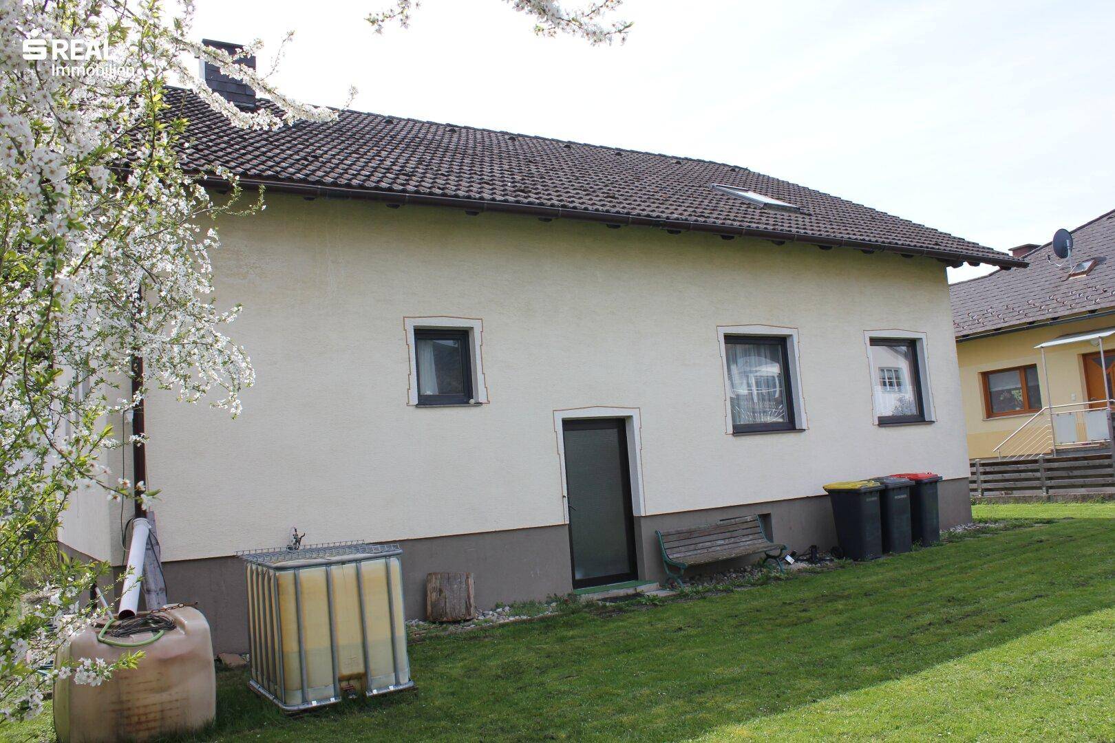 Hinterer Gartenbereich des Hauses mit Rasen, blühenden Bäumen und einem Wassertank.
