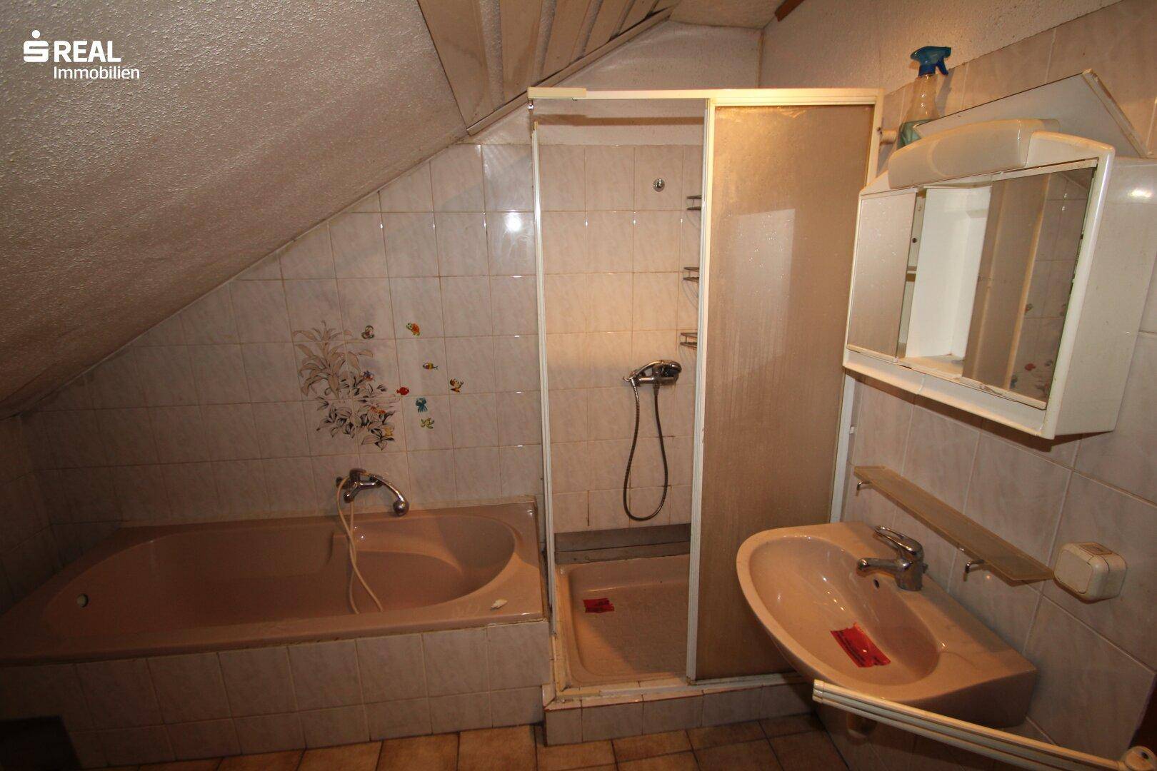 Badezimmer im Dachgeschoss mit Badewanne, Duschkabine und schrägen Wänden.
