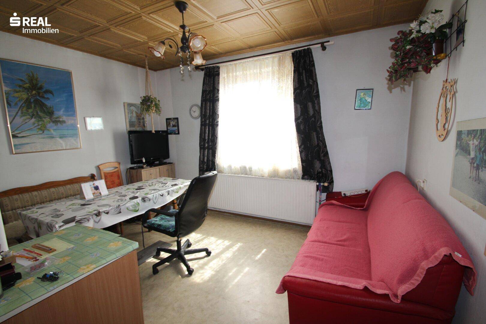 Gemütliches Wohnzimmer mit Sofa, Tisch und einem Fenster, das viel Tageslicht hereinlässt.
