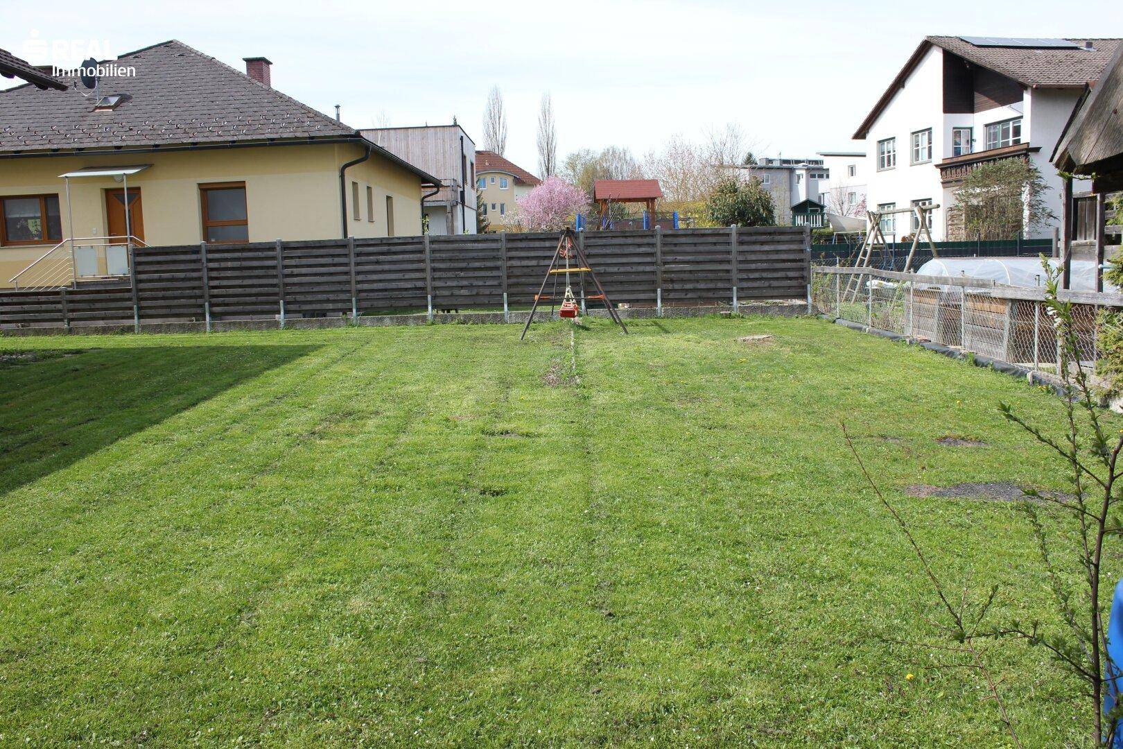 Großer, sonniger Garten mit Rasenfläche und einem Schaukelgestell für Kinder.
