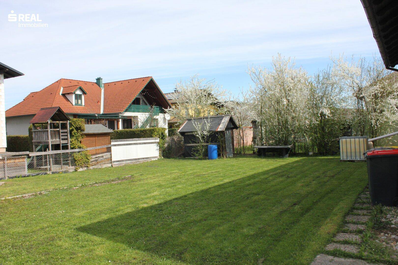Weitläufiger Gartenbereich mit gepflegtem Rasen und Blick auf benachbarte Häuser.