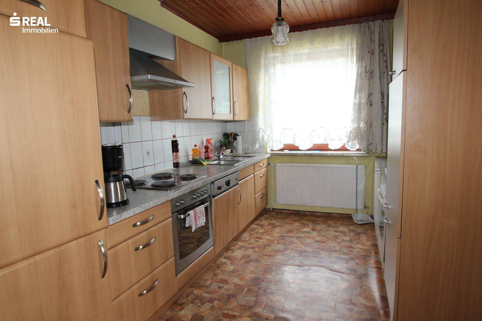 Traditionelle Küche mit Holzschränken, Fliesenboden und einem Fenster mit Vorhängen.