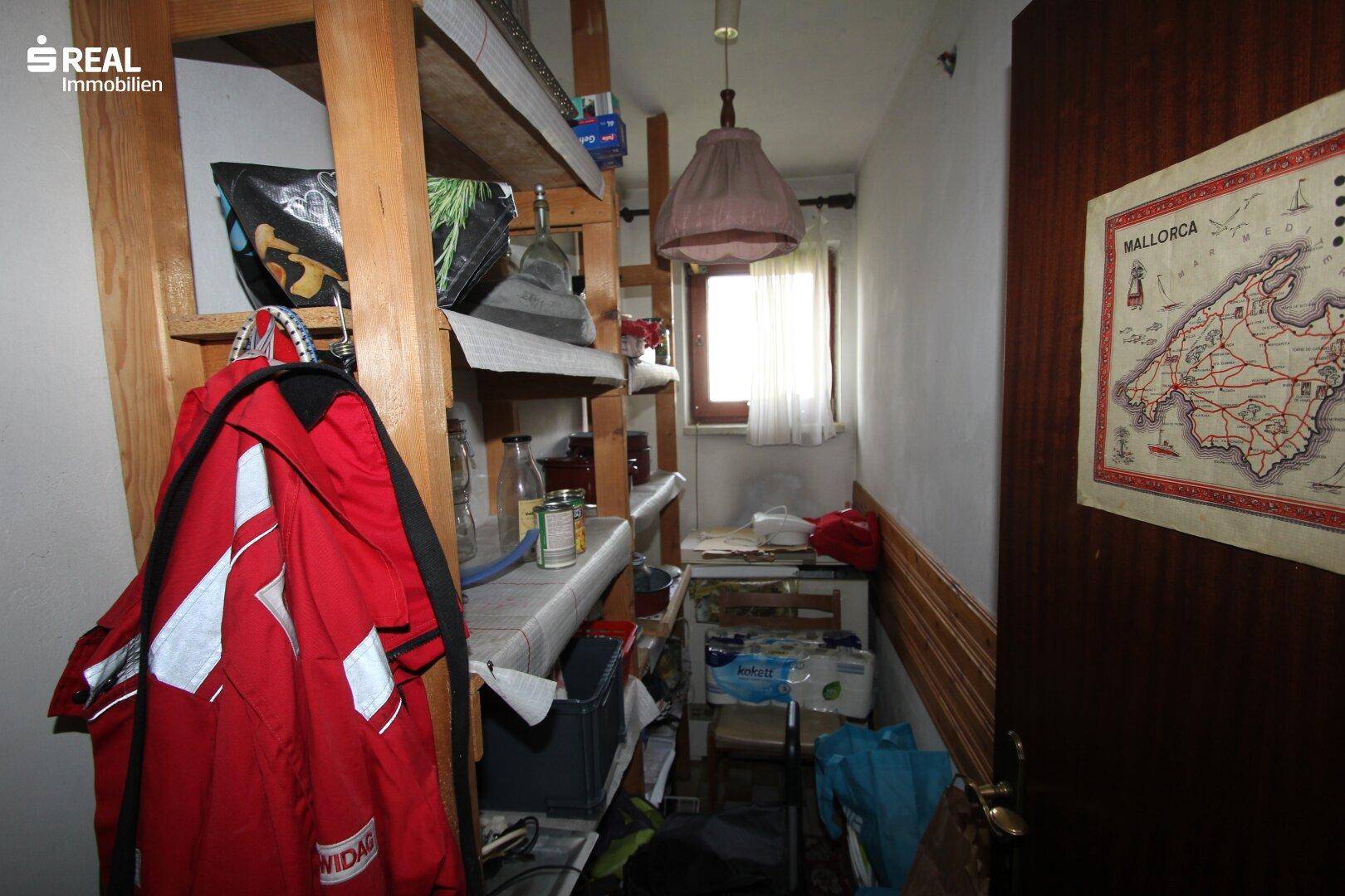 Kleiner Abstellraum mit Holzregalen, Fenster und verschiedenen gelagerten Gegenständen.