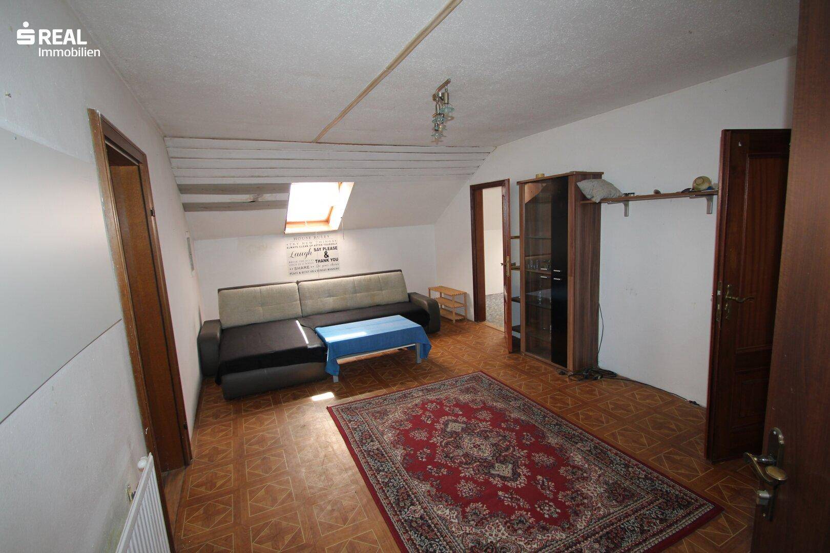 Geräumiges Wohnzimmer im Dachgeschoss mit Dachfenster, Sofa und Teppichboden.