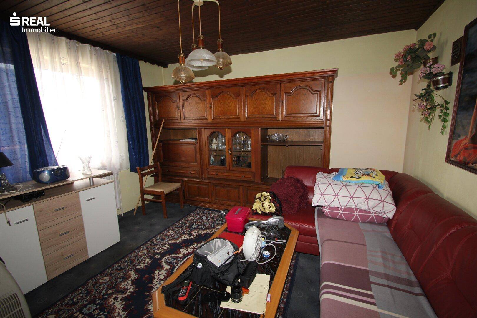 Wohnzimmer mit traditionellen Holzmöbeln, rotem Sofa und einem gemusterten Teppich.