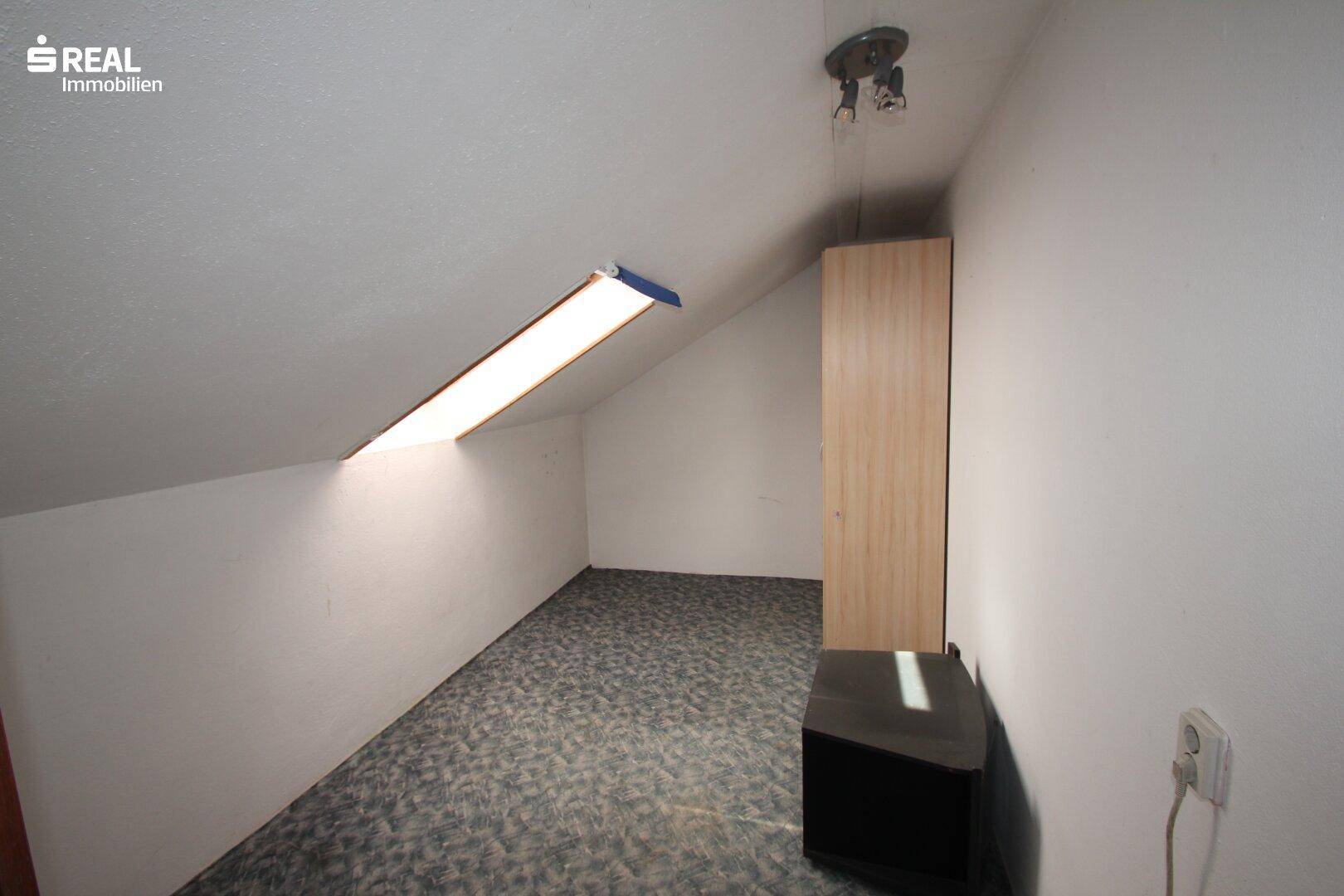 Weiteres Dachgeschosszimmer mit schrägen Wänden, Dachfenster und Teppichboden.