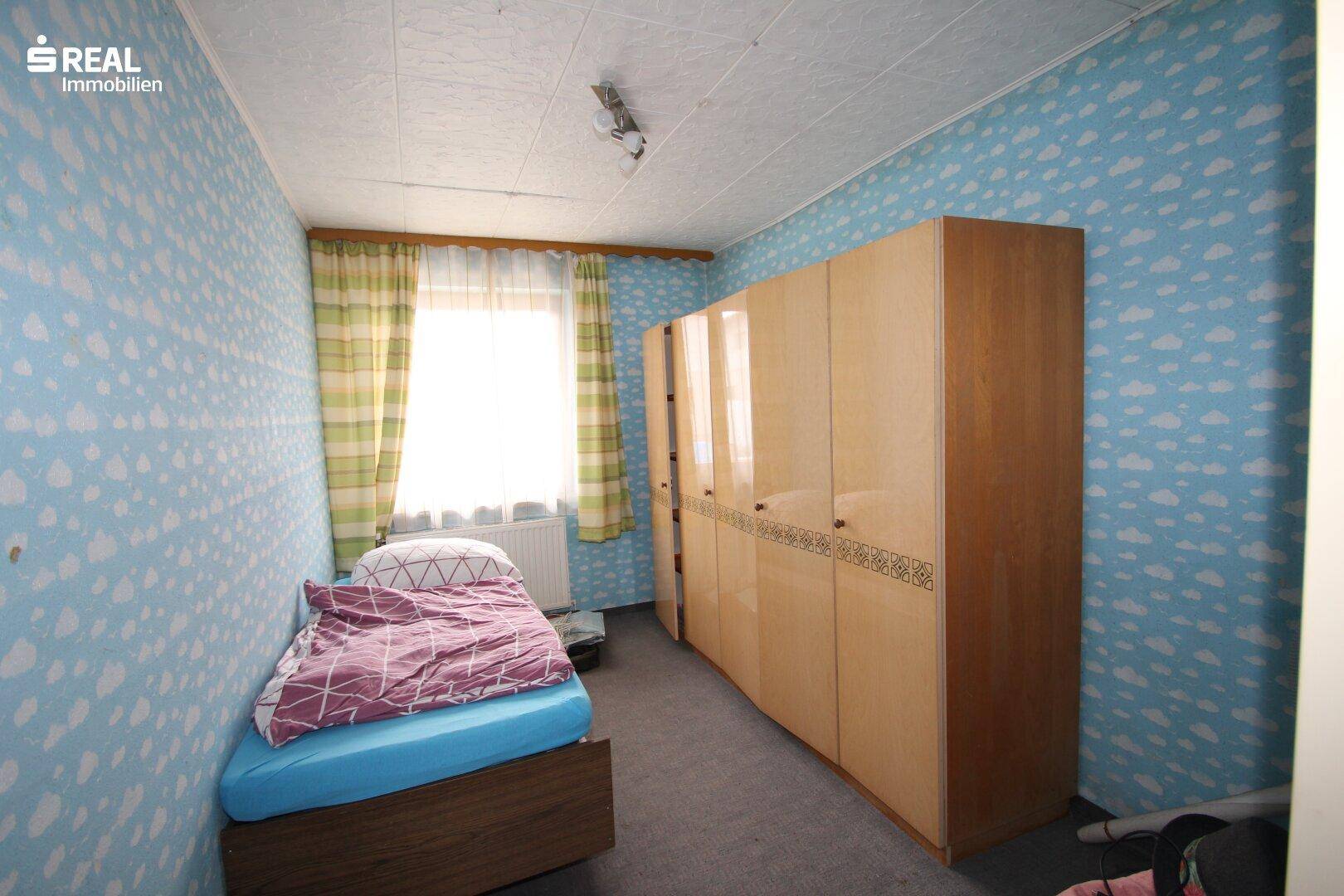 Kinderzimmer mit blauer Wolken-Tapete, Einzelbett und einem großen Kleiderschrank.