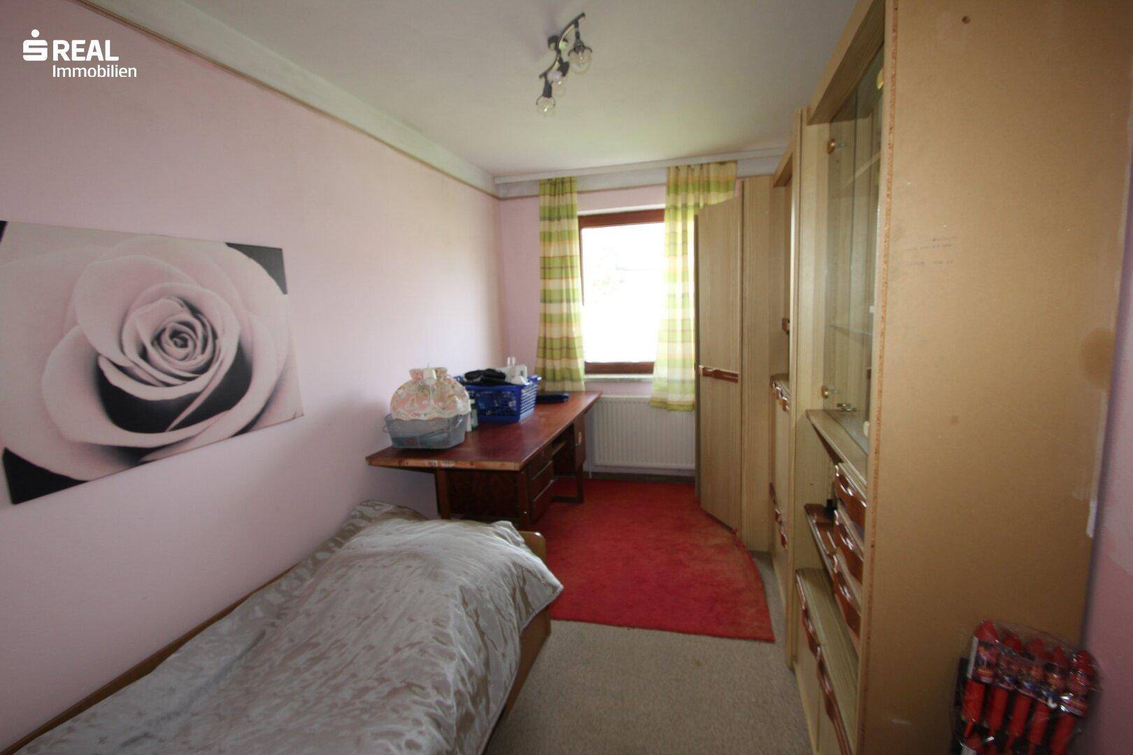 Helles Zimmer mit rosa Wänden, Einzelbett und einem Schreibtisch am Fenster.
