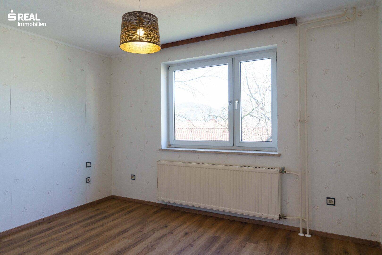 Helles Zimmer mit Laminatboden, Heizkörper und einem großen Fenster.