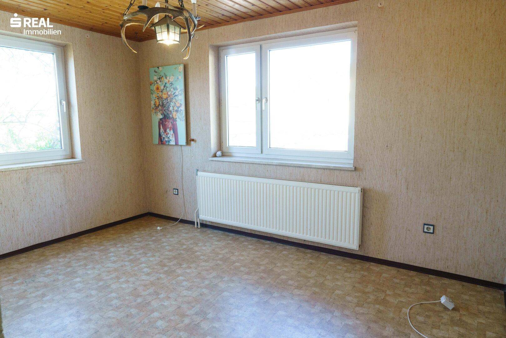 Zimmer mit gemustertem Boden, zwei Fenstern und einem Heizkörper.