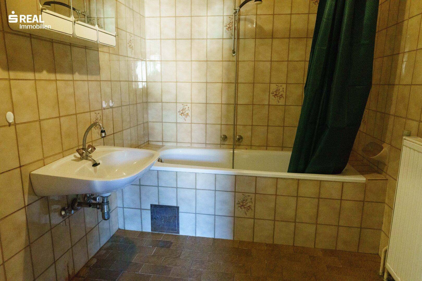 Badezimmer mit beigefarbenen Fliesen, Badewanne mit Duschvorhang und einem einzelnen Waschbecken.