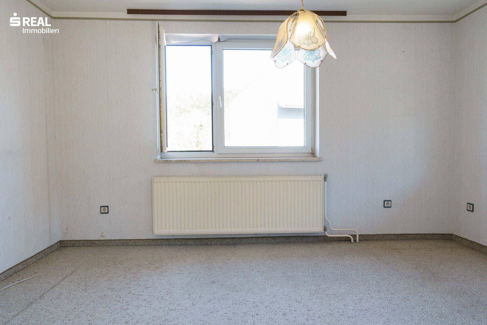 Leeres Zimmer mit hellem Boden, Heizkörper und einem Fenster.