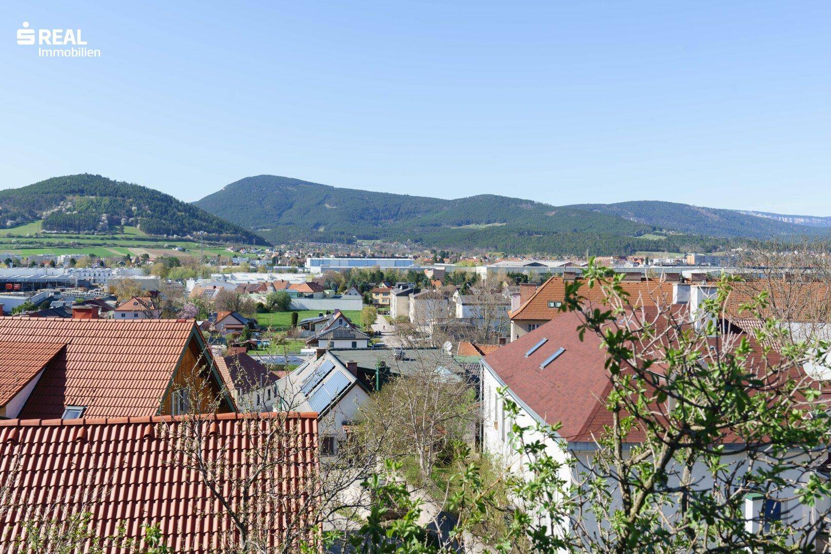 Weitläufiger Ausblick über die Dächer einer Stadt und die umliegende Berglandschaft.
