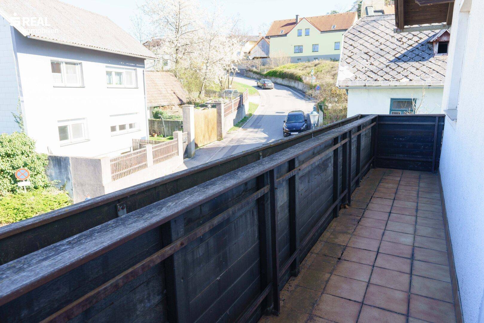 Balkon mit Fliesenboden und Holzgeländer, der einen Blick auf die Straße bietet.