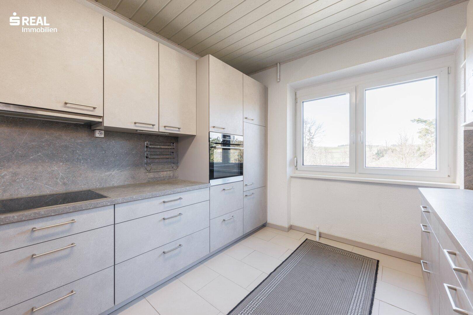 Moderne Küche mit hellgrauen Schränken, Fliesenboden und Fenster.
