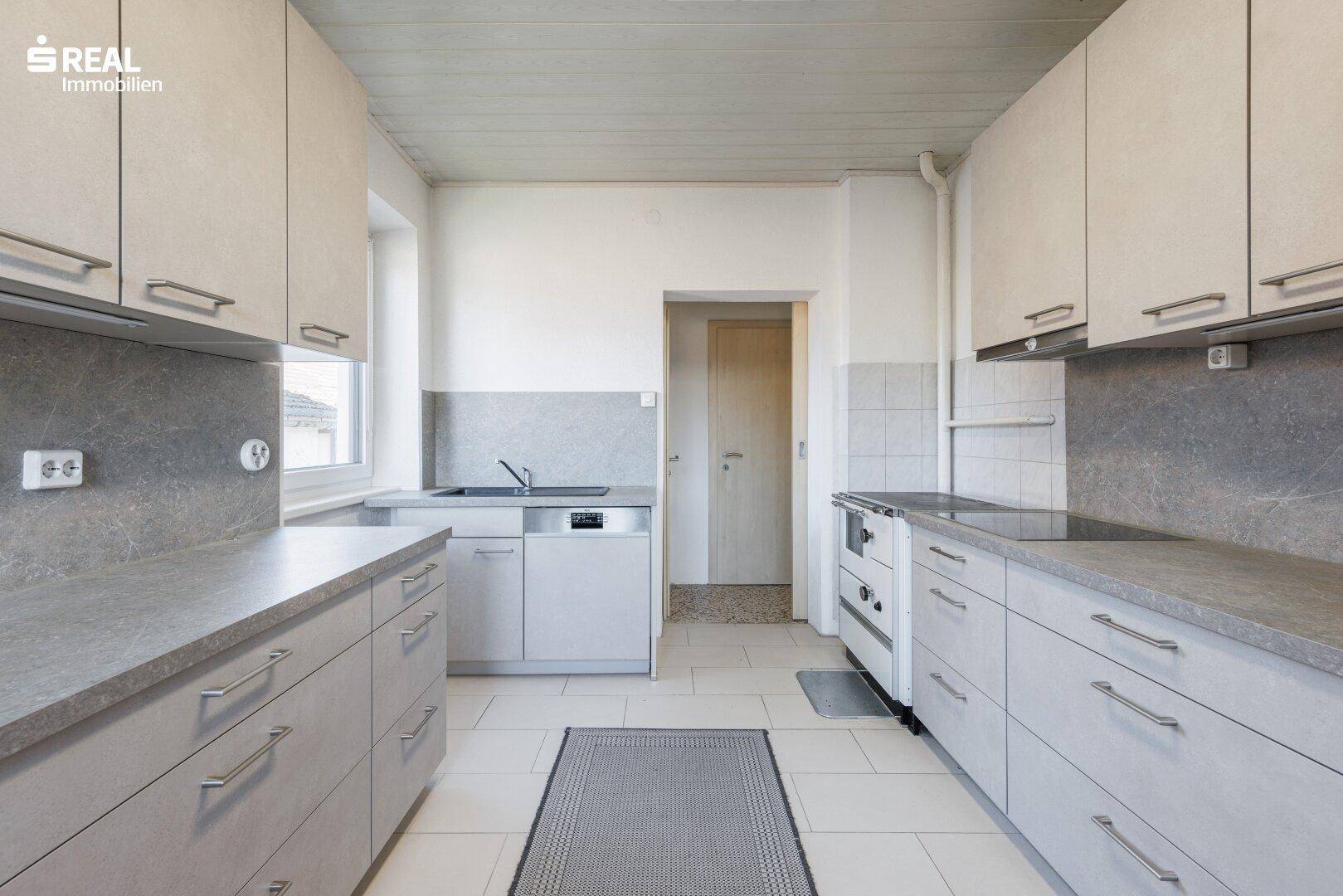 Funktionale Küche mit modernen grauen Schränken, Fliesenboden und Fenster.
