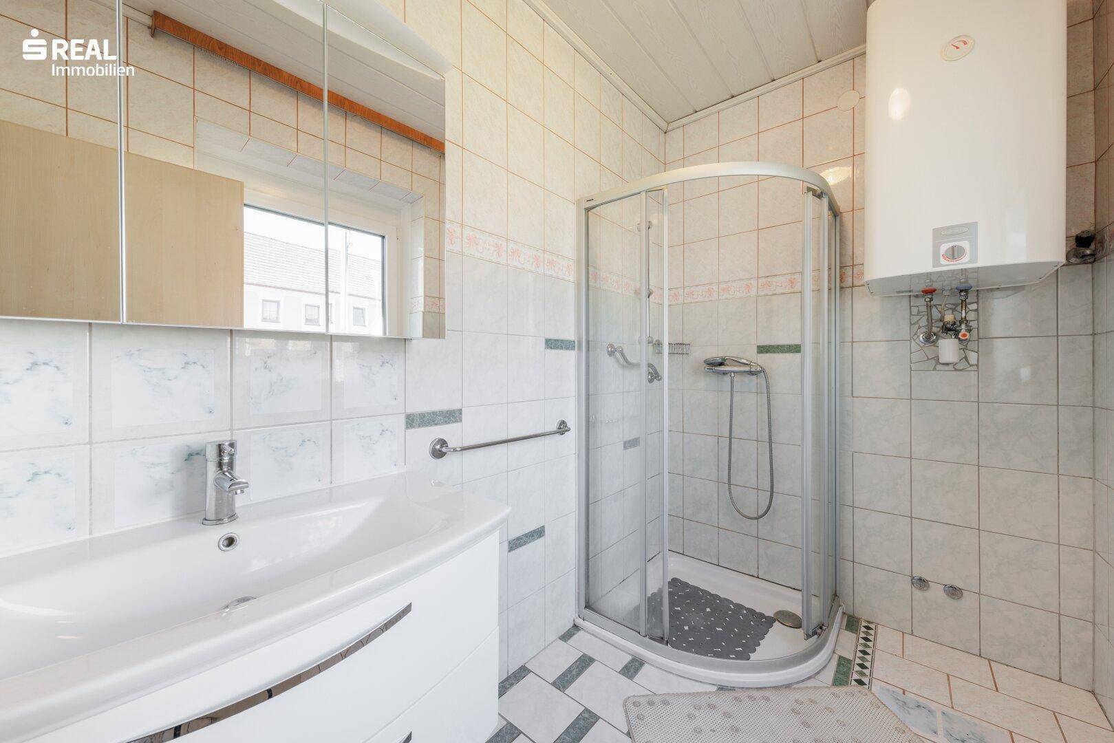 Gefliestes Badezimmer mit Dusche, Waschbecken und Spiegelschrank.