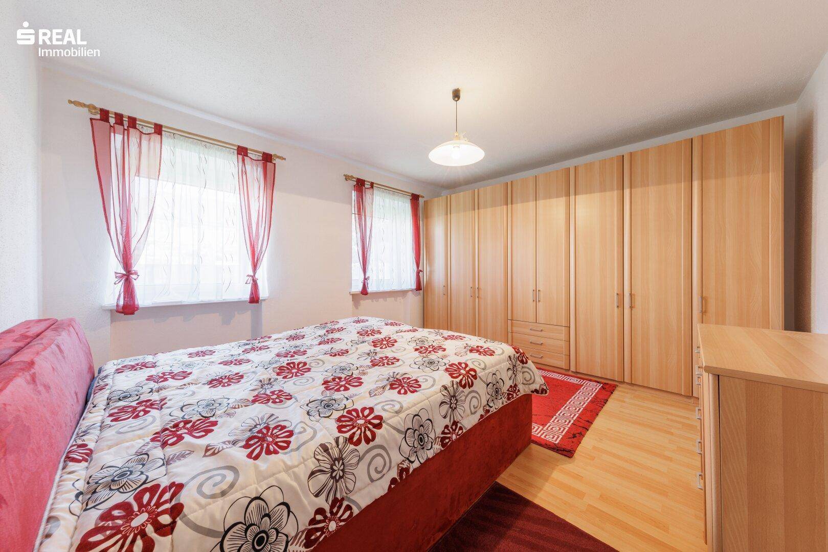 Geräumiges Schlafzimmer mit Holzschrank, Parkettboden und zwei Fenstern.
