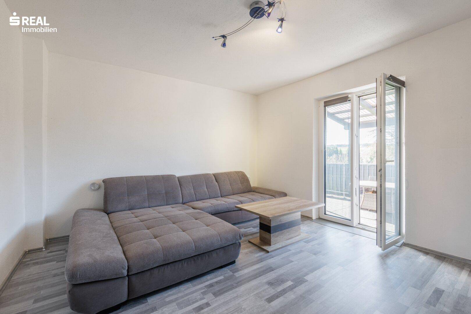 Helles Wohnzimmer mit modernem Sofa, Laminatboden und Zugang zum Balkon.