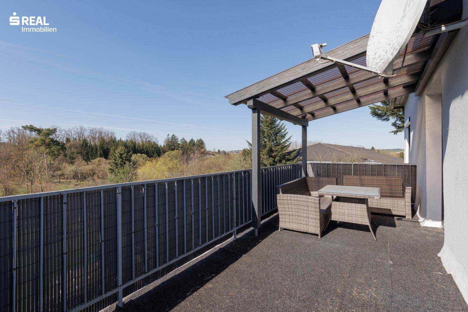 Überdachter Balkon mit Sitzgelegenheiten und weitem Blick ins Grüne.