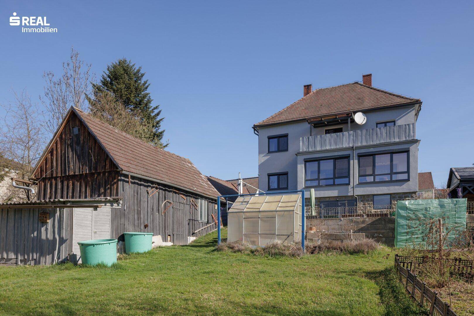 Garten mit Gewächshaus, Schuppen und Blick auf das Wohnhaus.