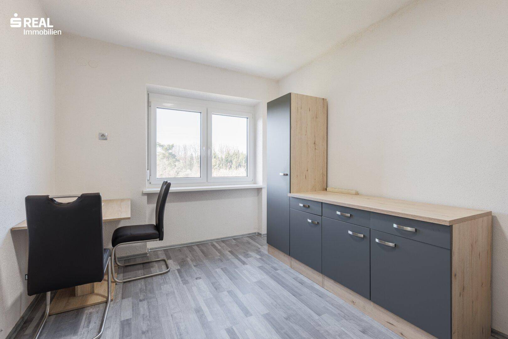 Arbeitszimmer mit Laminatboden, Schrank und Fenster mit Blick ins Grüne.